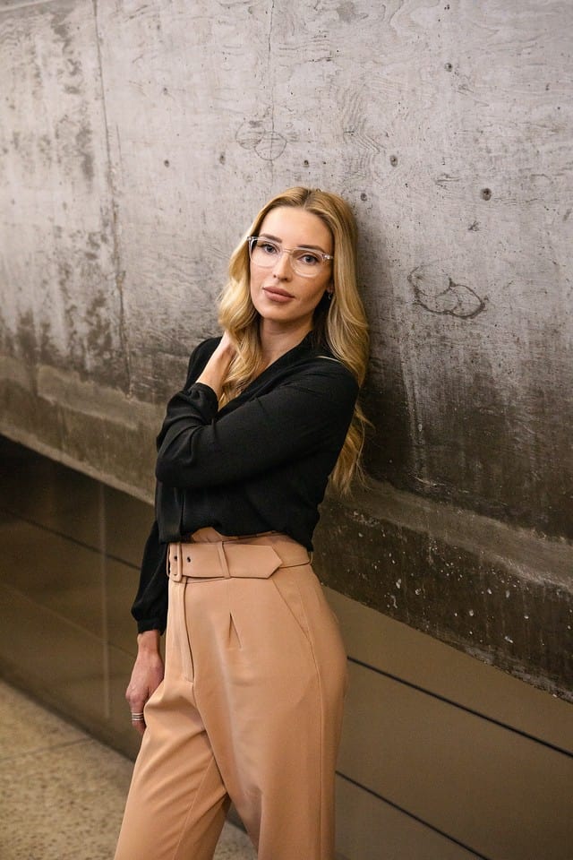 woman wearing a black shirt, standing gracefully while leaning against a wall