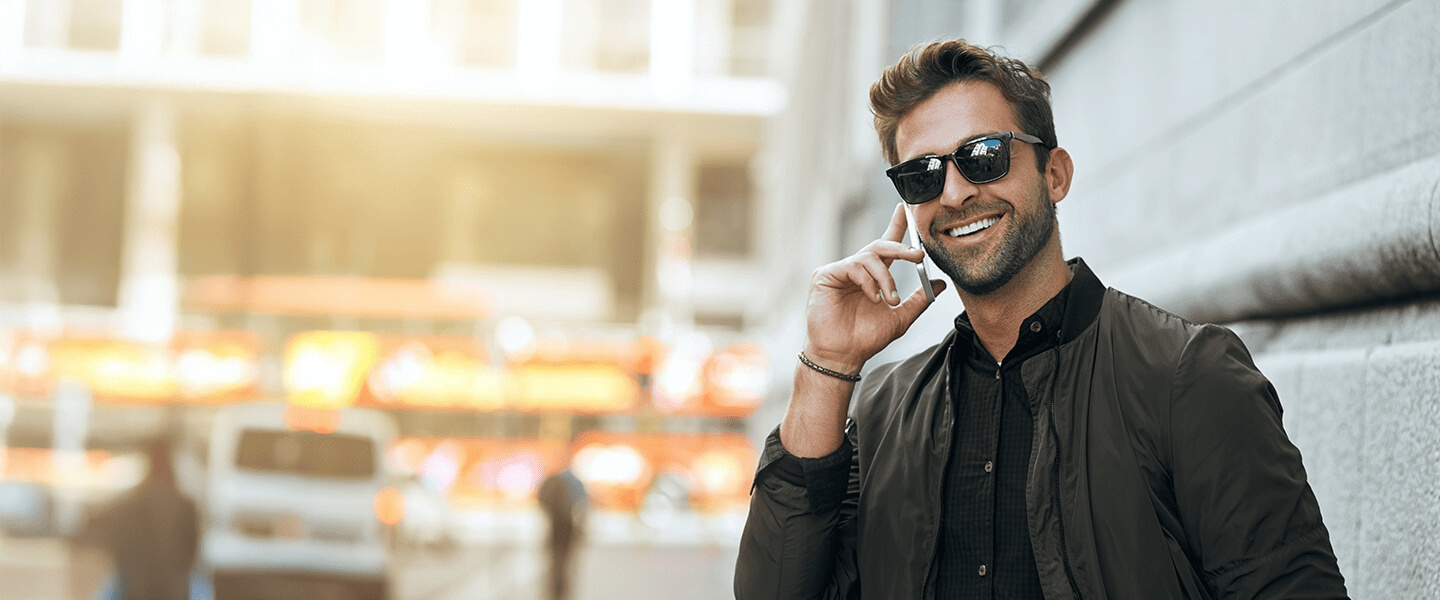 Smiling man wearing sunglasses and talking on the phone outdoors